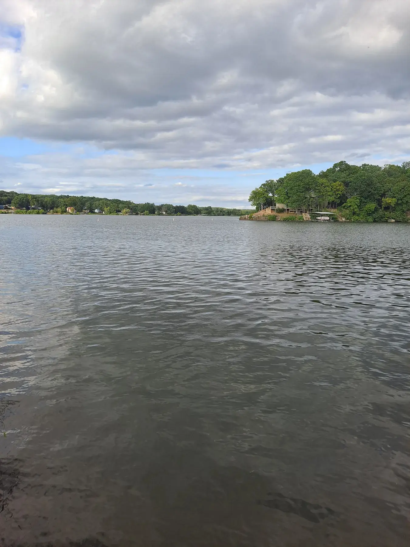 Wide lake under a dramatic cloudy sky with tree-lined shore
