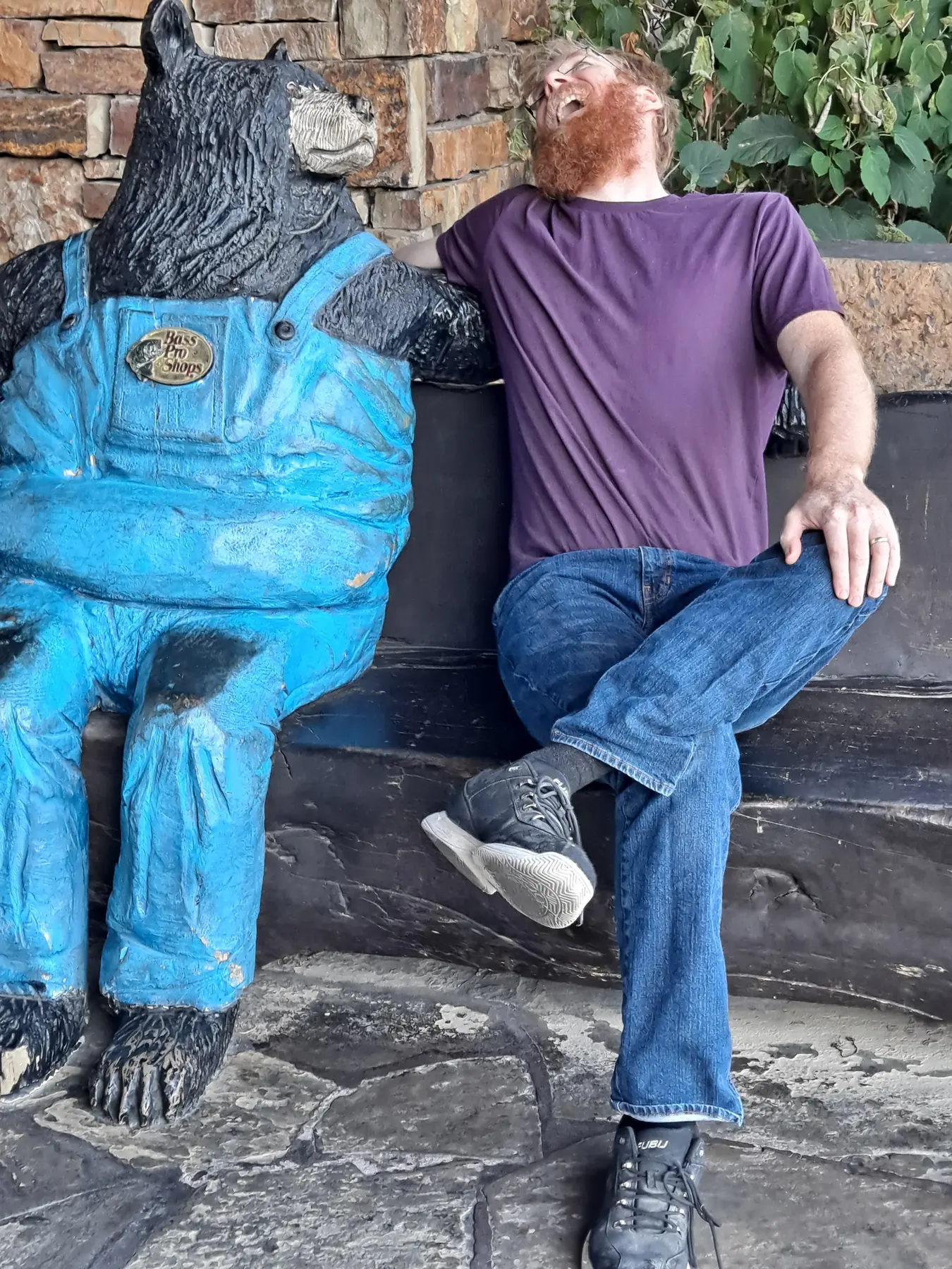 Life-size carved black bear statue dressed in blue overalls greeting visitors outside a shop