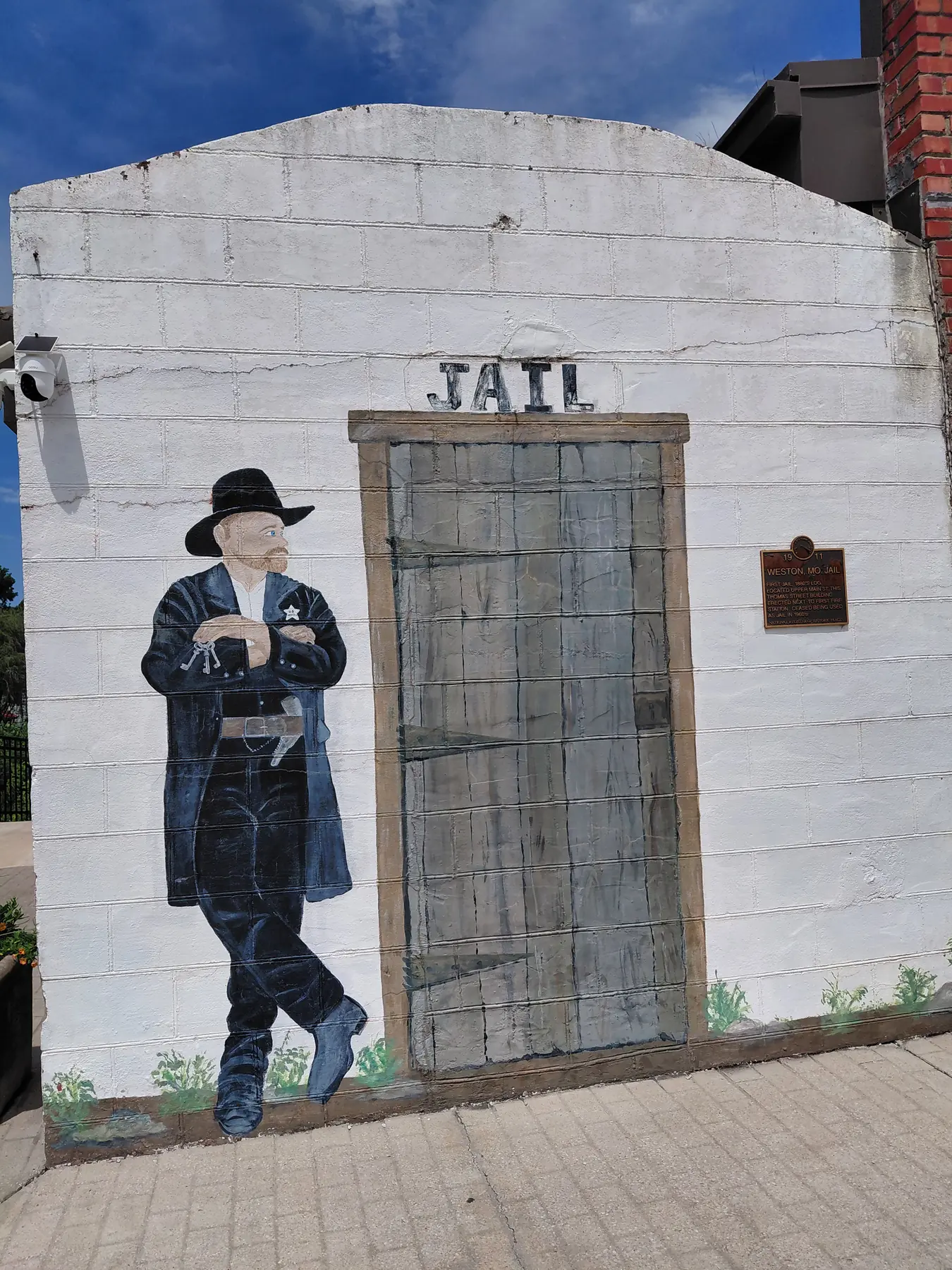 Painted mural of an old jail with a sheriff on a white brick wall