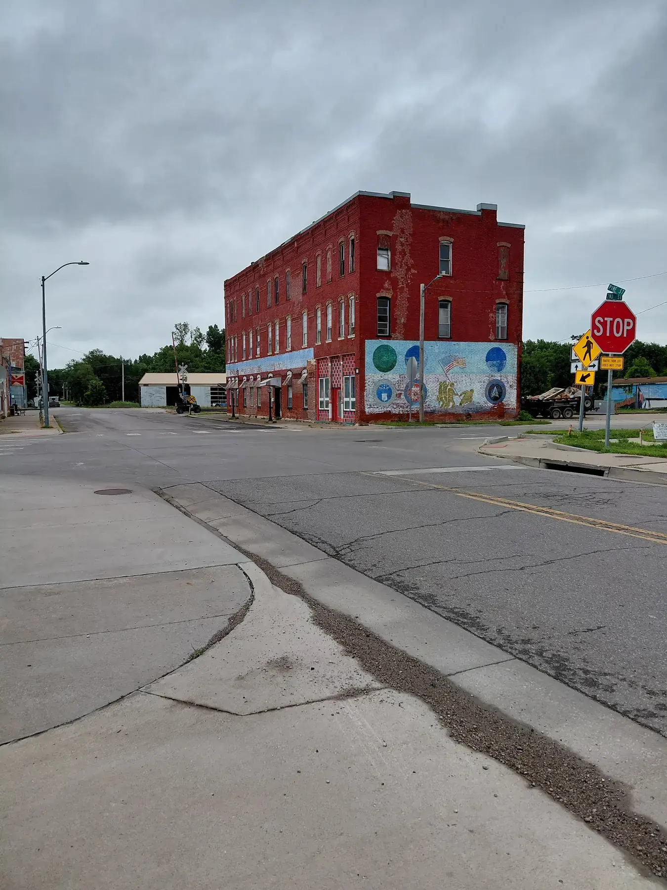 Historic red brick corner building with a mural at a quiet crossroads
